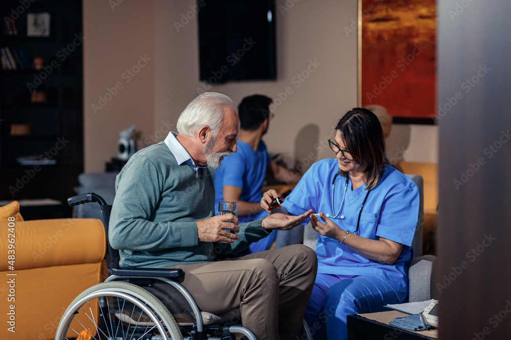 Nurse helps an senior man in a wheelchair to take medication at nursing home.