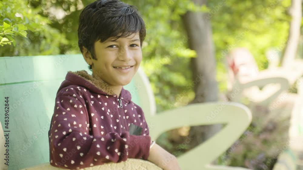 smiling Indian kid in winter wear sitting at park by looking camera - Concept positive emotion, Happiness and relaxation smiling Indian kid in winter wear sitting at park by looking camera - Concept positive emotion, Happiness and relaxation