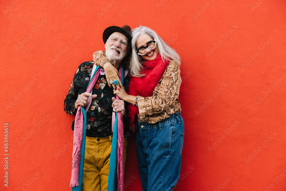 Fototapeta premium Happy elderly couple smiling cheerfully against a red wall