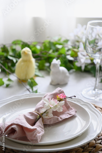 Easter table setting with yellow chick, festive decorations, fresh flowers and eggs. Elegance dinner at home interior. Close up.