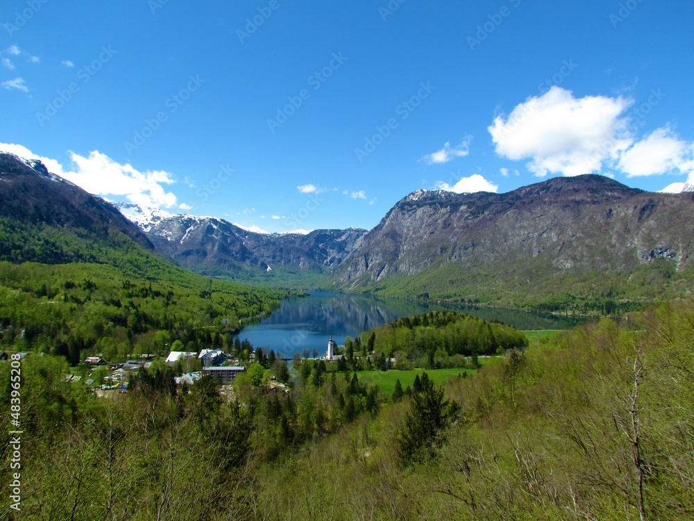 Beautiful view of Bohinj lake and the village of Ribcev Laz in Gorenjska, Slovenia with the surrounding forests in bright green spring foliage and mountains rising above the lake