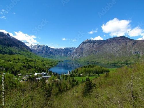 Beautiful view of Bohinj lake and the village of Ribcev Laz in Gorenjska, Slovenia with the surrounding forests in bright green spring foliage and mountains rising above the lake