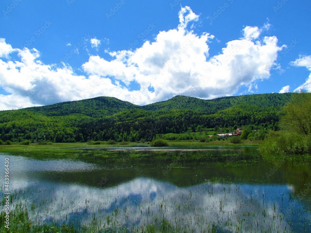 Scenic view of lake Cerknica and Javorniki hills in Notranjska, Slovenia with a reflection of the hills and the clouds in the lake