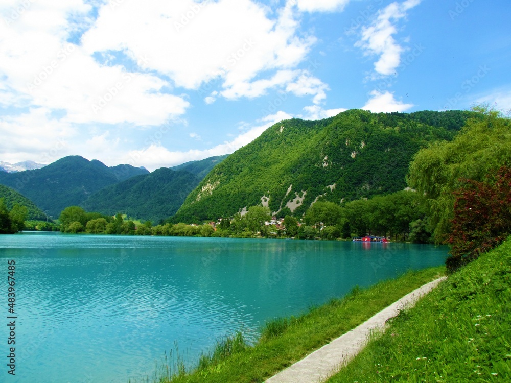 Walking trail next the lake at Most na Soci in Littoral region of Slovenia with forest covered mountains and hills behind