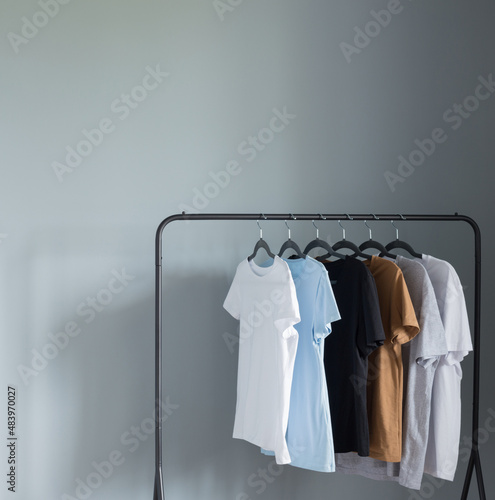 T-shirts of neutral colors on  black hanger against  gray wall
