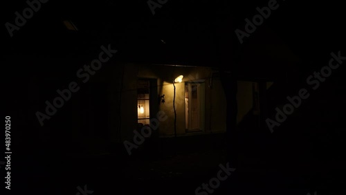 Facade and front door of cottage at night illuminated by small light. France.