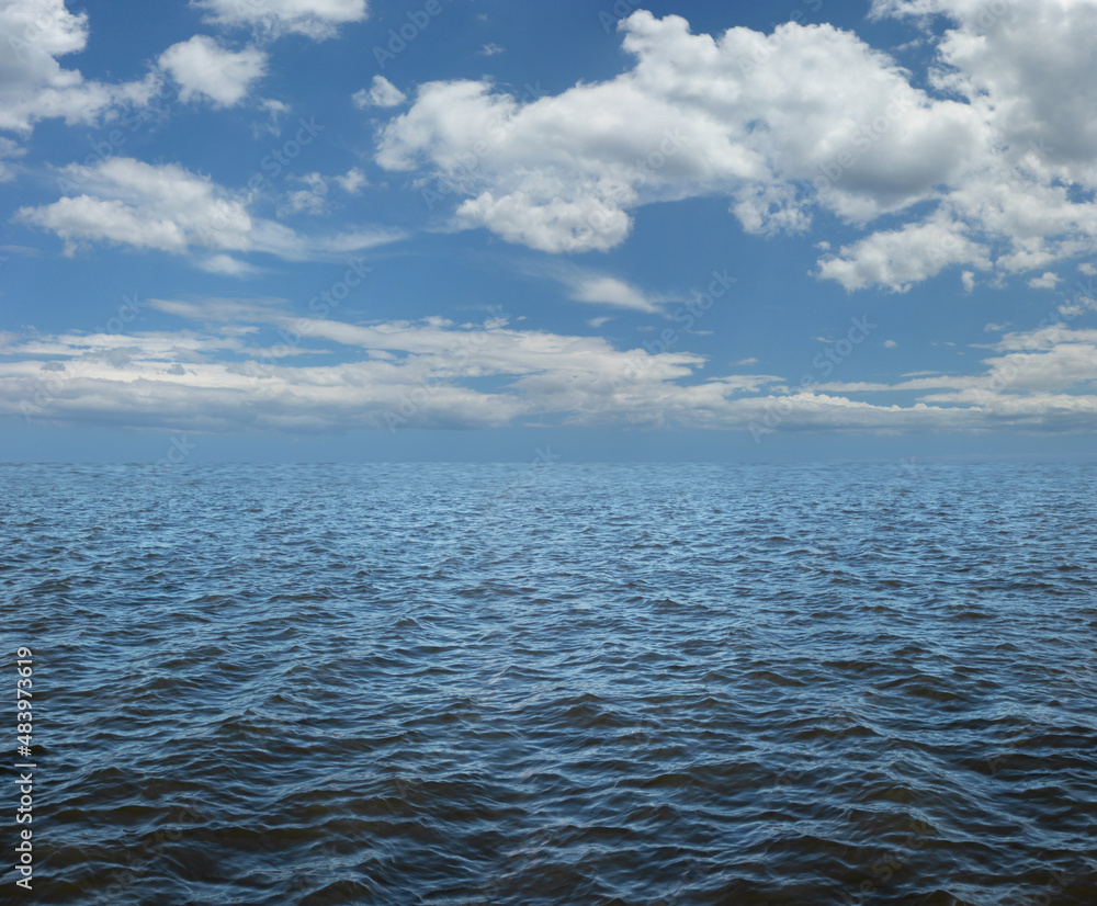 Obraz premium Simple rippling water and fluffy clouds nautical message background - blue sky and puffed clouds with ocean beneath ideal for a marine theme fishing, vacation, nature or weather message 