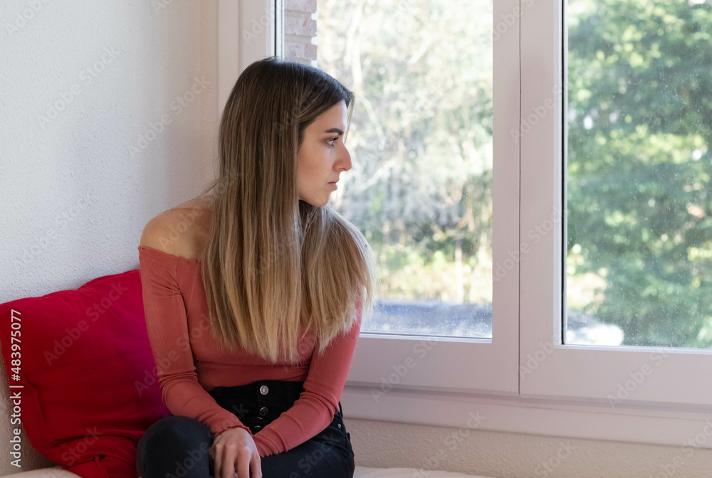Young woman and blonde thoughtful and depressed looking out the window Young woman and blonde thoughtful and depressed looking out the window