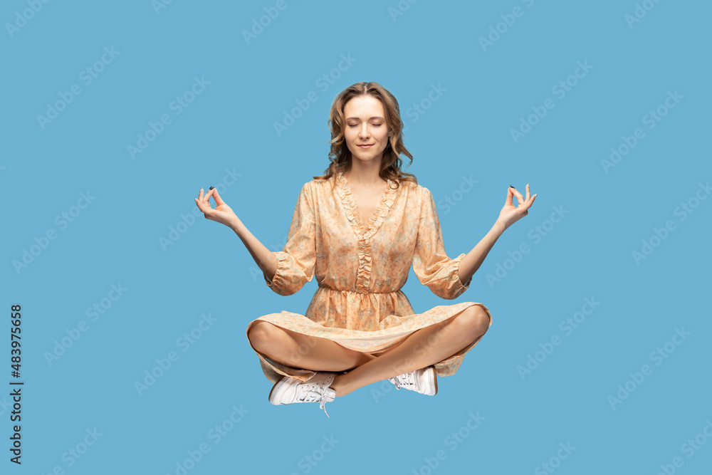 Hovering in air. Calm peaceful relaxed girl ruffle dress levitating with mudra gesture hands up, closed eyes, meditating sitting in yoga position. indoor studio shot isolated on gray background Hovering in air. Calm peaceful relaxed girl ruffle dress levitating with mudra gesture hands up, closed eyes, meditating sitting in yoga position. indoor studio shot isolated on gray background