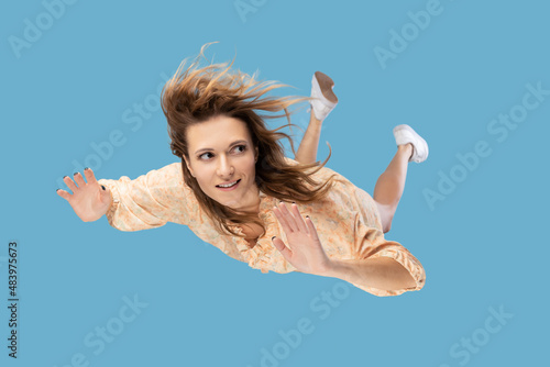Fototapeta Beautiful young woman levitating in mid-air, falling down and her hair messed up soaring from wind, model flying hovering with dreamy peaceful expression