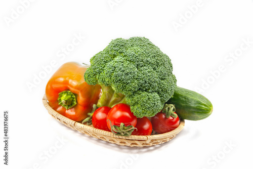Fresh broccoli, cucumber, pepper and tomatoes on a wicker basket on white background