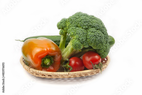 Fresh broccoli  cucumber  pepper and tomatoes on a wicker basket on white background