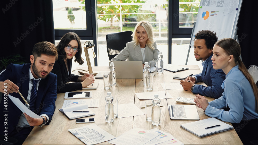 Fototapeta premium young manager pointing at document near interracial business people in meeting room