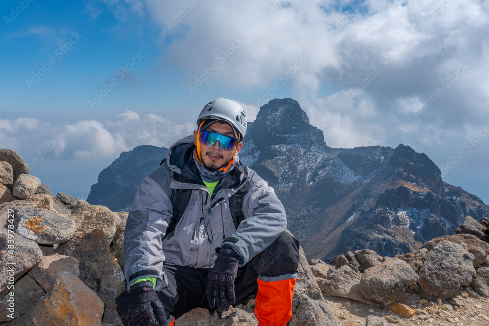 portrait of a climber with helmet and goggles in front of mountains