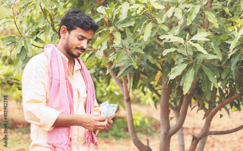 Fotografie happy young indian former counting money at farm land - concept of successful forming business, agricultural profit and finance