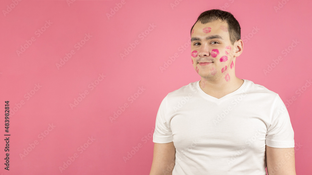 Attractive young man full of kiss marks on his face.Traces of lipstick on the man's face.Pink background, banner, copy space.Womanizer, playboy,ladies man,philanderer,lovelace. Attractive young man full of kiss marks on his face.Traces of lipstick on the man's face.Pink background, banner, copy space.Womanizer, playboy,ladies man,philanderer,lovelace.