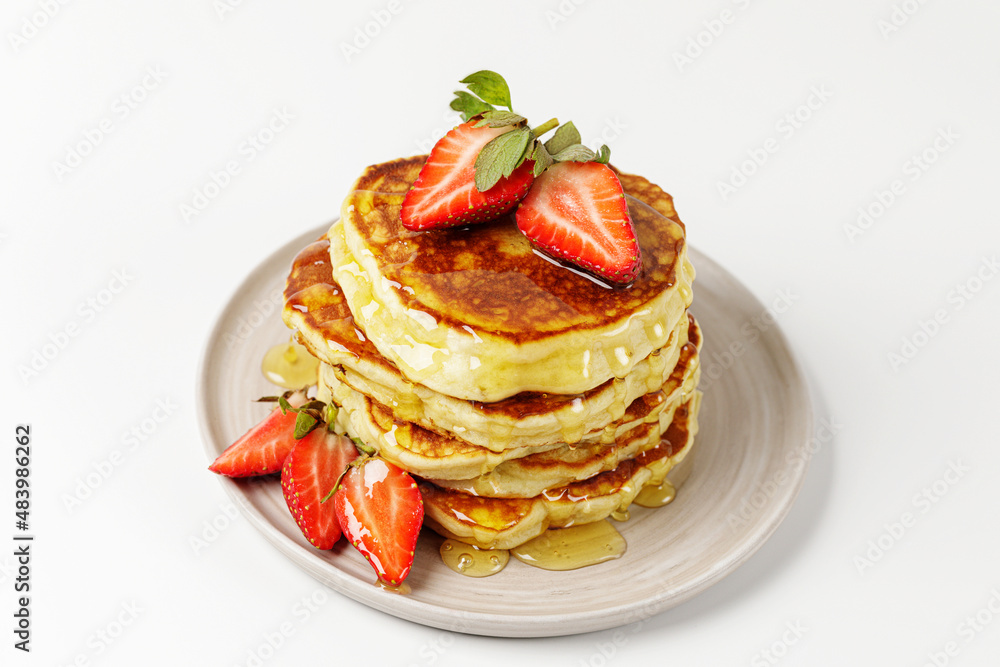 A stack of pancakes with honey and fresh strawberries in plate on white background. Delicious healthy dessert for breakfast. A stack of pancakes with honey and fresh strawberries in plate on white background. Delicious healthy dessert for breakfast.