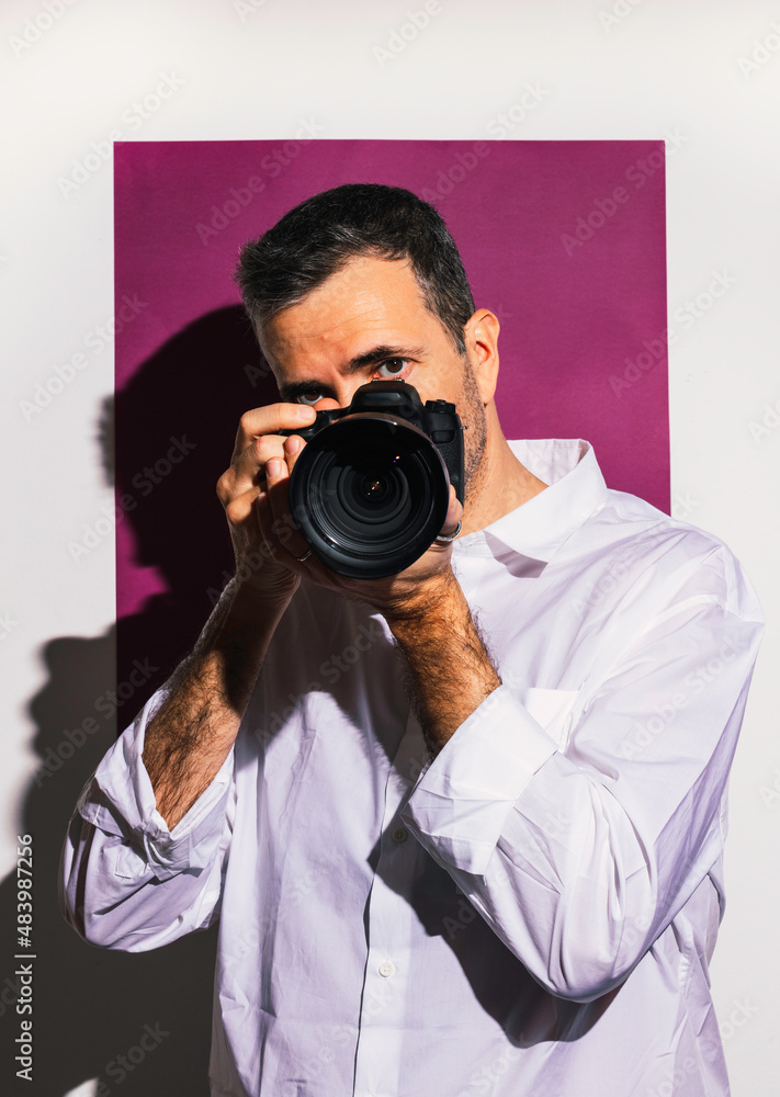 Elegant man taking a photo with his camera on fuchsia pink background Elegant man taking a photo with his camera on fuchsia pink background