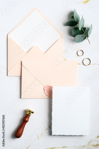 Elegant wedding stationery set. Wedding invitation card template, pastel pink envelopes, wax seal stamp, rings, eucalyptus on marble table. Flat lay, top view, copy space.