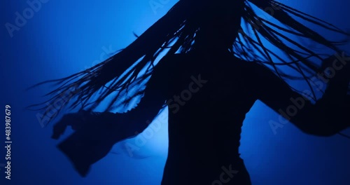Silhouette of young woman dancing in blue light and smoke photo