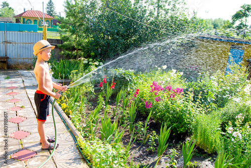 little gardener in a hat watering flowers on a hot summer day