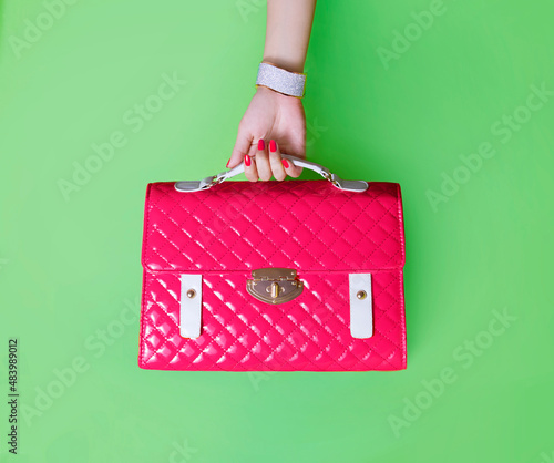 Red purse isolated on green background. Beautiful red nails and bracelet.