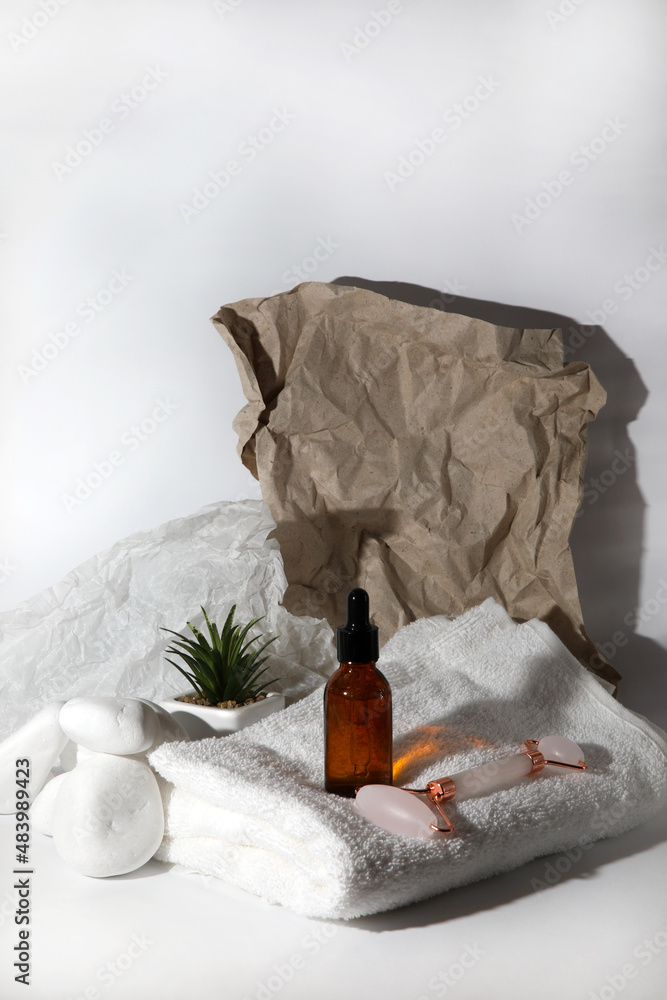Facial serum and roller on white towel on white background with craft crumpled paper Facial serum and roller on white towel on white background with craft crumpled paper