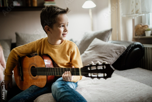 Young boy in yellow sweater playing the acoustic guitar at home. photo