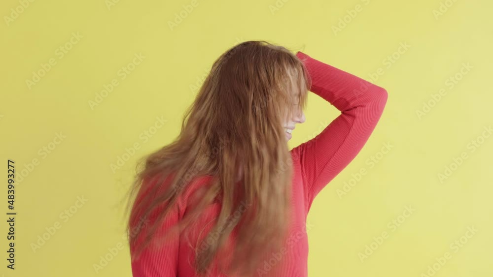 Energetic red-haired young woman happily dances and has an upbeat mood, expresses positive emotions, on yellow background. concept of people and emotions Energetic red-haired young woman happily dances and has an upbeat mood, expresses positive emotions, on yellow background. concept of people and emotions