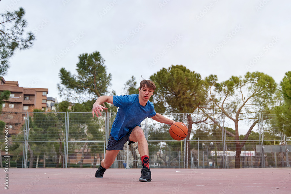 Obraz premium young athlete training outdoors. caucasian man playing basketball on a court, practicing dribbling with the ball.