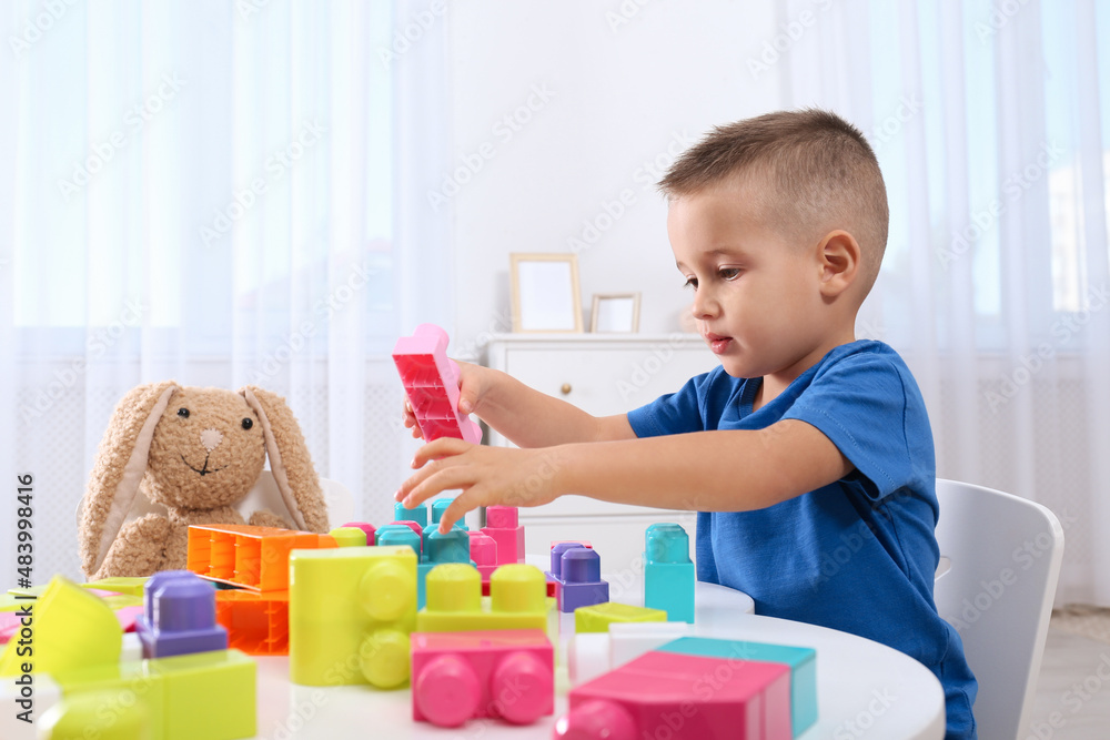 Cute little boy playing with colorful building blocks at table in room Cute little boy playing with colorful building blocks at table in room