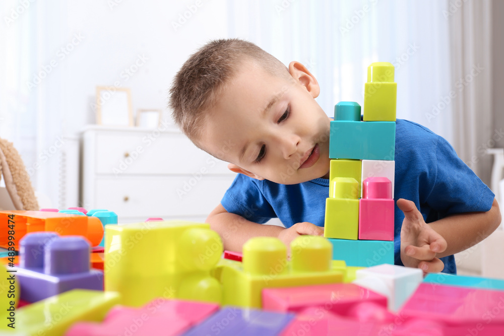 Cute little boy playing with colorful building blocks at table in room Cute little boy playing with colorful building blocks at table in room