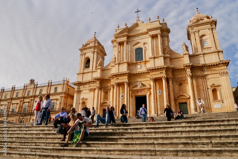 Noto, Sicily, 31.03.2018. People sitting on stairs in front of Baroque cathedral San Nicolo in Noto, UNESCO World Heritage Site. Sicily.