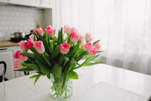 Bouquet of pink tulips in a transparent vase on the kitchen table. Flowers in the interior. International Women's Day 8 March.