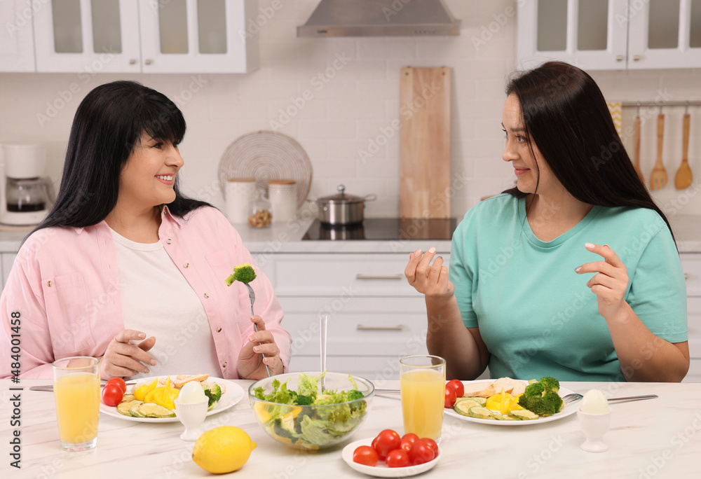 Happy overweight women having healthy meal together at table in kitchen Happy overweight women having healthy meal together at table in kitchen