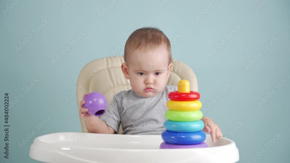 Toddler 15-25 months collects and disassembles a colored plastic pyramid sitting on a chair. Toddler 15-25 months collects and disassembles a colored plastic pyramid sitting on a chair.
