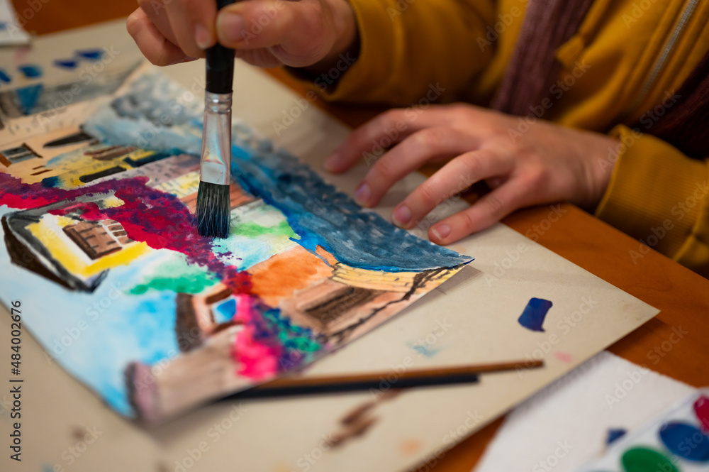 Fototapeta premium Brush in hand above watercolor painting. Colorful medieval city street on paper board.