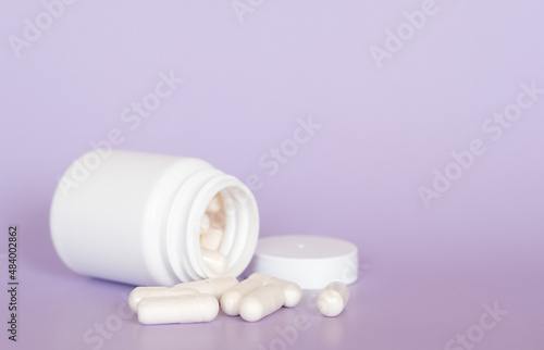 Close up white pills and capsules on purple background with copy space. Focus on foreground  soft bokeh. Pharmacy drugstore concept.