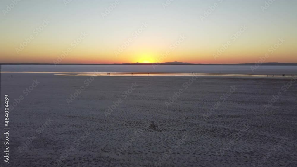 Flying toward sunset over a flat salt lake Tuz in Turkey with people walking on it