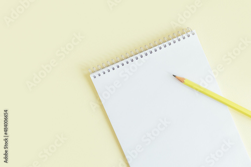 Notebook with blank page and pencil on a yellow pastel background.
