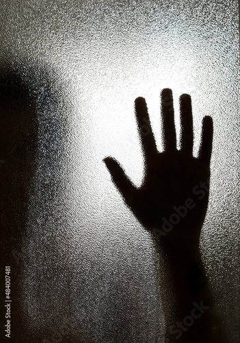 Silhouette of a hand on the glass in the shower.