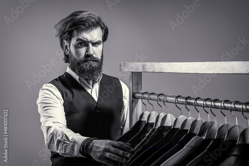 Man suit, tailor in his workshop. Male suits hanging in a row. Tailor, tailoring. Stylish men's suit. Handsome bearded fashion man in classical costume suit photo