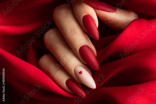 Canvas Print Matte red nails with small red heart on beige colour nail on the red fabric background