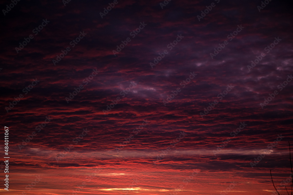 Bright colorful sunset sky with vivid smooth clouds illuminated with setting sun light spreading to horizon