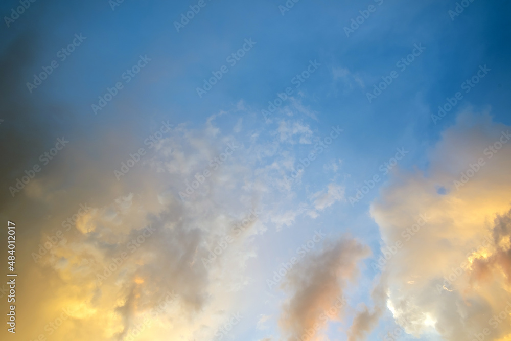 Dramatic moody sunset landscape with puffy clouds lit by yellow setting sun and blue sky