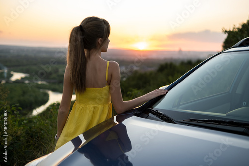Yong happy woman standing near her car enjoying sunset view of summer nature. Travel and getaway concept © bilanol