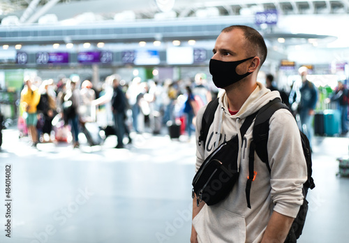 Young man in a protective mask with backpack standing in the airport or at the train station. The concept of safe travel during a pandemic. Copy space.