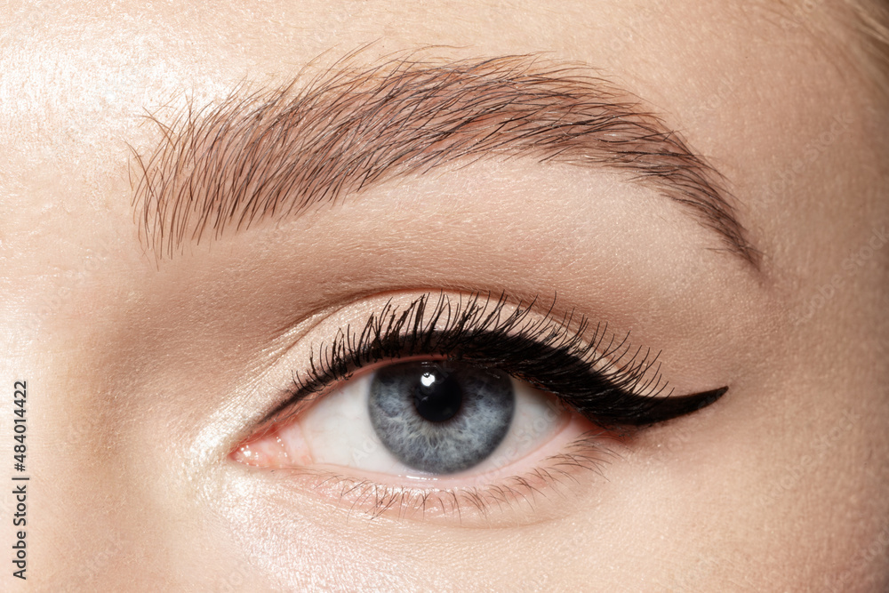 Obraz premium Beautiful blue eye of young woman with black eyeliner and long eyelashes 