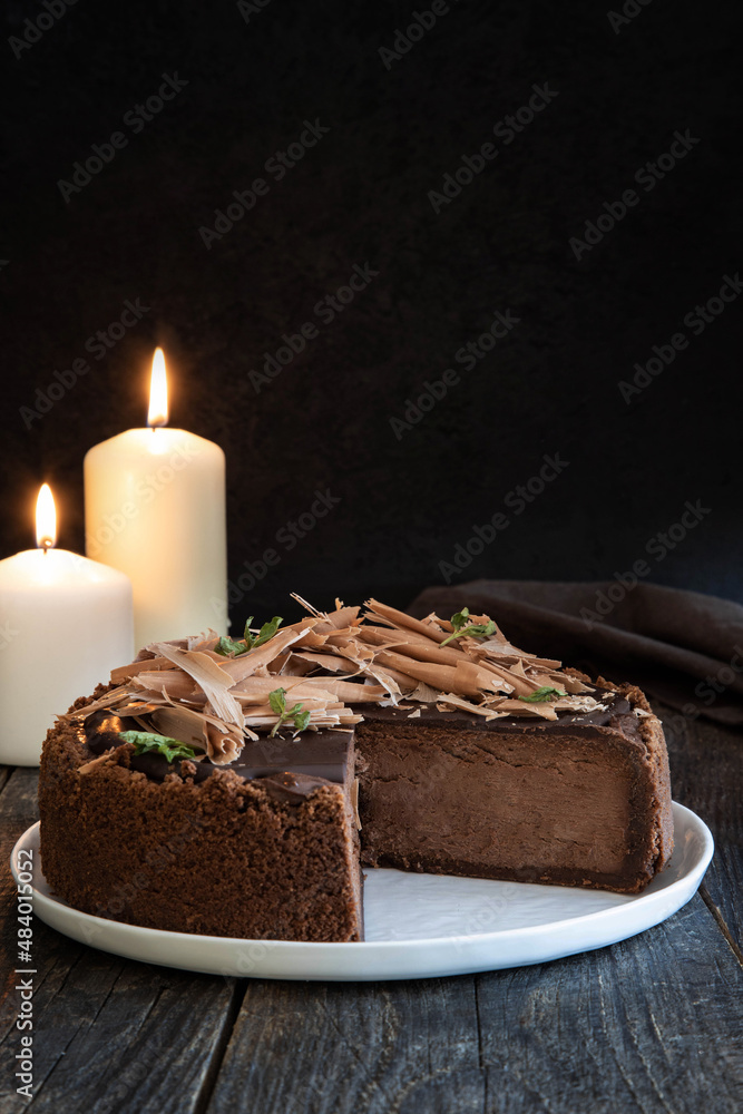 Chocolate cheesecake or sponge cake in cut on a dark wooden table by candlelight.