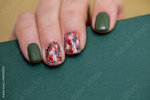 Beautiful creative female manicure in orange and green colors. Drawing with gel polish on nails. Woman's hand holding an old book close-up.